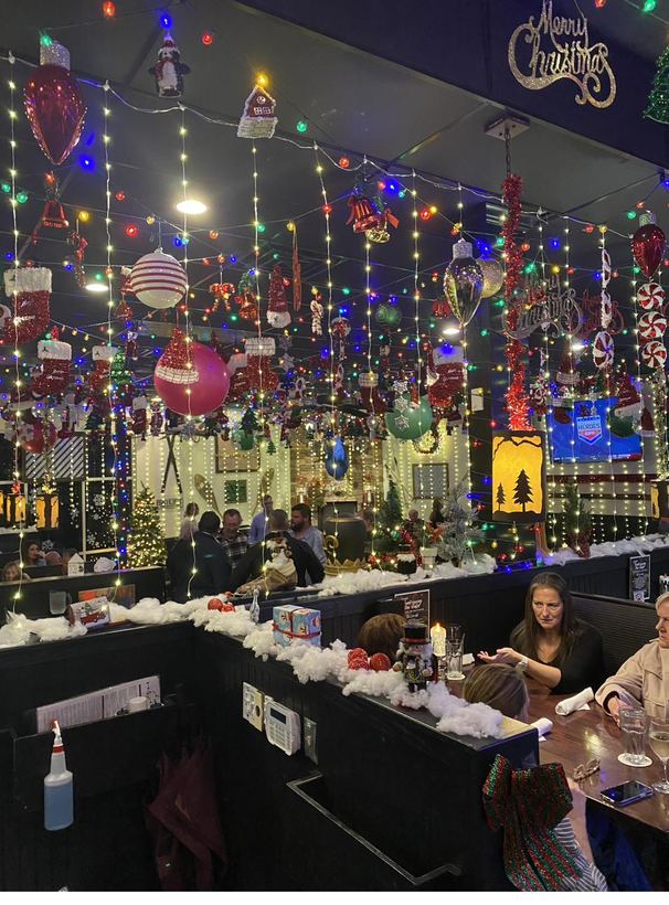 A long dining hall draped top to bottom in holiday lights and ornaments