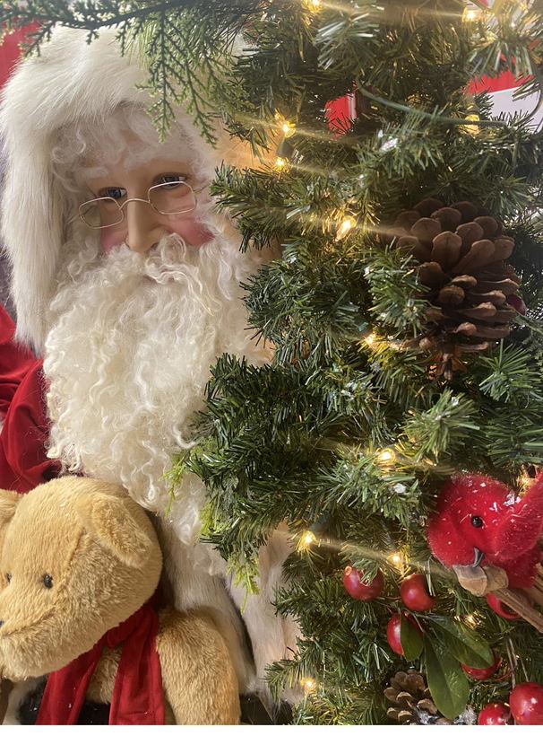 Santa standing beside a brightly lit Christmas tree